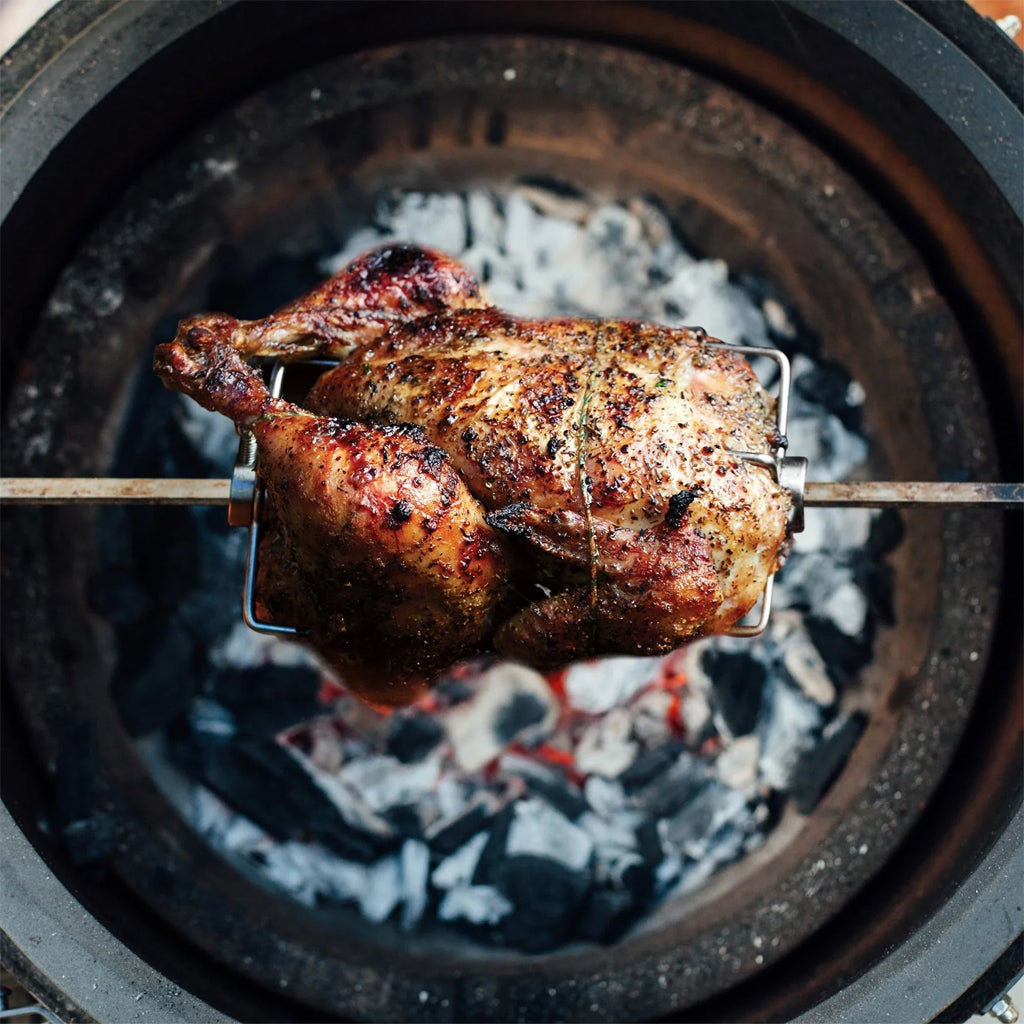 Top-down view of a whole chicken roasting on a Joetisserie Rotisserie Kit inside a Kamado Joe grill over hot charcoal.